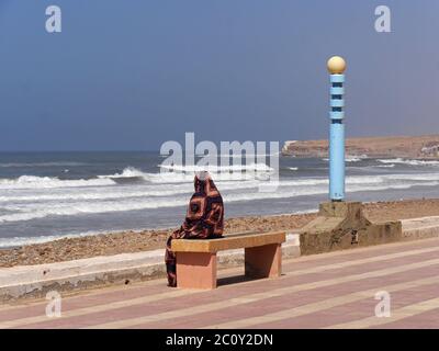 Muslim sitting on a bench on the Atlantic coast in Aglou Plage, Morocco Stock Photo
