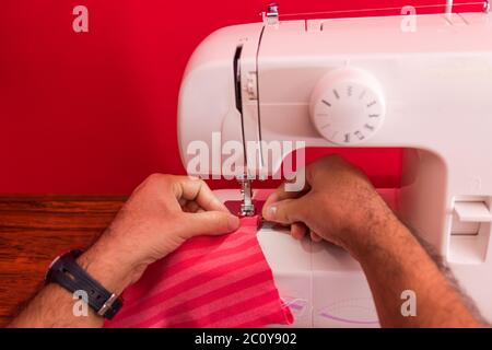 Hand of man using a sewing machine. Concept of National Sewing Machine day, june 13. Hands sewing a piece of fabric. Close up photo. Red background wi Stock Photo