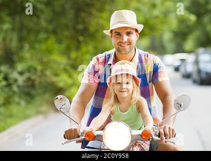 Happy young father and little daughter riding a vintage scooter in the street wearing hats Stock Photo