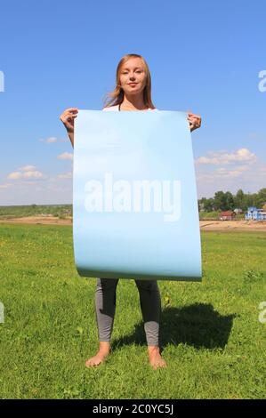 A beautiful long-haired girl on the green grass on the lawn holds an empty blue poster. Layout for design, place for text, copy space. Stock Photo