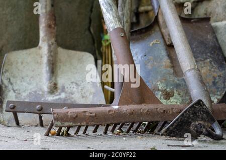 Closeup of various rusty garden tools on the ground. Hoe, rake, various shovels with adhering earth. Hand tools for gardening and farming. Selective f Stock Photo
