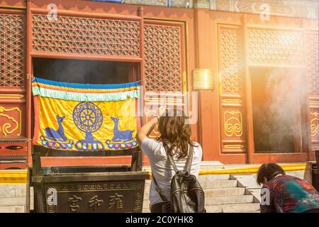 Asian woman worshipping with incense sticks at a colorful Buddhist temple Stock Photo