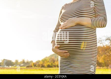 Woman standing on meadow and holding her pregnant belly in the beautiful afternoon light Stock Photo