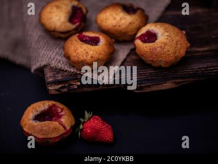 Cupcakes with white cream and strawberry on vintage blanket over black wooden background with fresh strawberries. Stock Photo