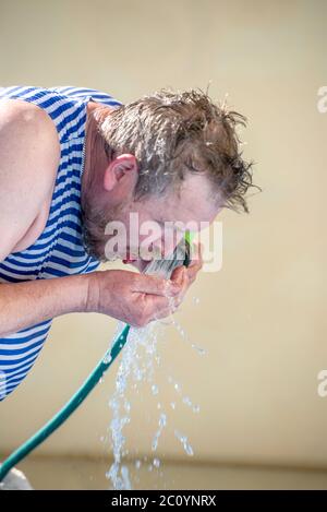 man drinks water from a hose on a hot day Stock Photo