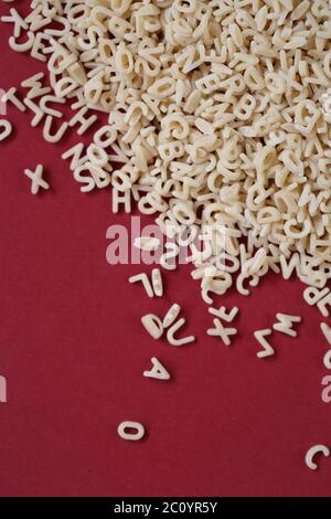 Pasta letters heap close-up on a bright burgundy background..Dry uncooked pasta. kids food.Pasta tiny english letters background.letters pattern. Stock Photo