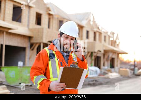 Caucasian engineer talking by smartphone and looking at blueprint. Stock Photo