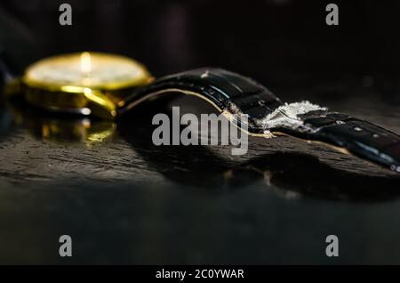 Used and worn out black belt of a golden watch on a worn out black table. Stock Photo