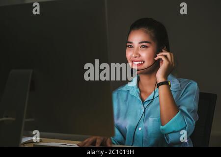 Asian Female customer care service smiling and working hard late in night shift at office, call center department, worker and overtime, teamwork with Stock Photo