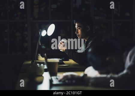 Asian businessman working hard late with his technology laptop in office, customer service and call center department, hard worker and overtime, her c Stock Photo