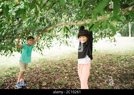 little girls smile while hanging on tree branches while playing together in the garden Stock Photo