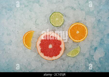Close up fresh juicy citrus fruits slices, pink grapefruit, orange and green lime, over background of crushed ice, elevated high angle view, directly Stock Photo
