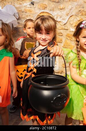 Portrait of a little girl hold bucket for candies standing in a group of friends and smiling Stock Photo