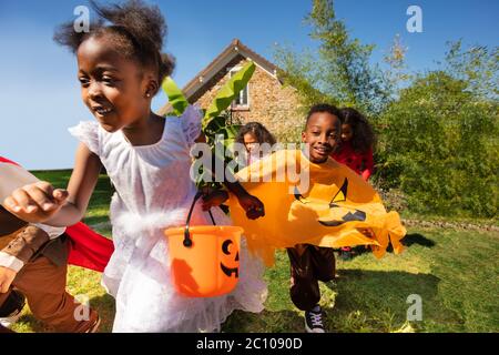 Close portrait of a group of little children run in Halloween costume on the lawn before the house holding hands Stock Photo