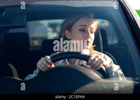 Woman drives her car for the first time, tries to avoid a car accident, is very nervous and scared, worries, clings tightly to the wheel. Inexperience Stock Photo