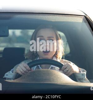 Woman in stress and confusion after an accident, damaged another car during parking, drives her car for the first time. Driver with open mouth and ast Stock Photo