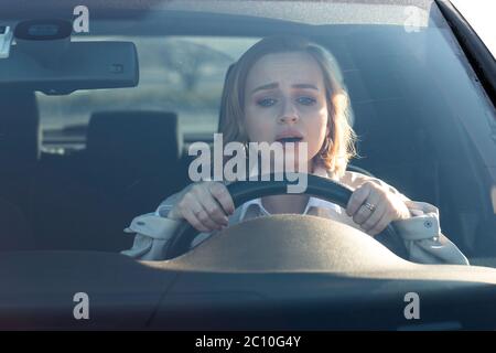 Woman drives her car for the first time, tries to avoid a car accident, is very nervous and scared, worries, clings tightly to the wheel. Inexperience Stock Photo