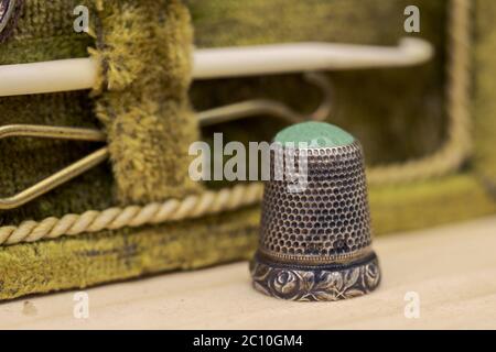 Antique thimble made of iron and green glaas standing on wooden board with old sewing kit in blurred background Stock Photo