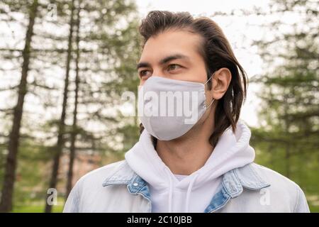 Handsome middle-aged man in cloth mask looking around while walking in forest during coronavirus pandemic Stock Photo