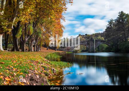 Fall foliage and medieval Roman bridge reflected on the water in the Galician village of Allariz, Ourense. Stock Photo