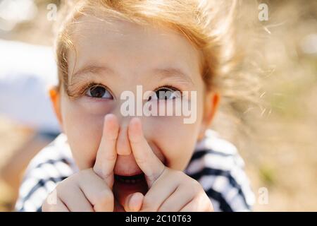 Little girl pinching nose with index fingers, grimasing, playing with her face Stock Photo