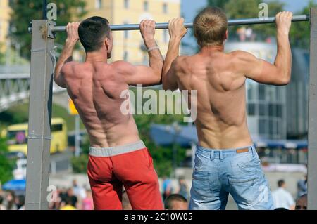 Two young men pulling bodies up on a horizontal bar set on a street, people watching. June 3, 2018. Kiev, Ukraine Stock Photo