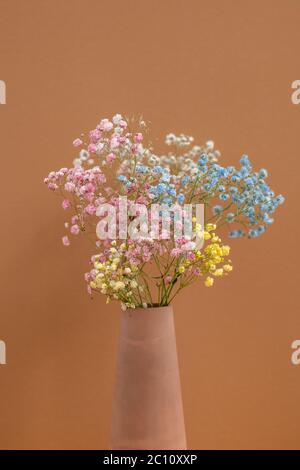 Bouquet of multi-color dried flowers in handmade clay vase standing on background of brown wall as a part of interior of domestic room Stock Photo