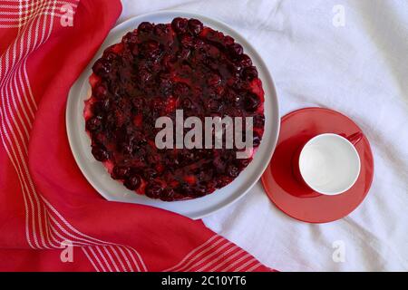 Homemade no baked cake with mascarpone cheese cream, fresh cherries and jelly  on a white plate,  red small plate and empty cup Stock Photo