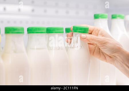Hands of contemporary mature female consumer taking plastic bottle of kefir with green lid from shelf on dairy products display Stock Photo