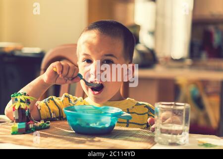 The boy 4 years eats porridge. Children's table. The concept of the child's independence. the boy is breakfasting with an appetite on the kitchen Stock Photo