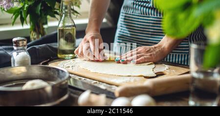 Woman is rolled the dough for making noodles. Concept of cooking delicious food in a cozy home atmosphere Stock Photo