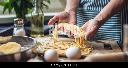 Woman is carefully holding raw fresh homemade noodles in her hands. Concept of process of cooking handmade pasta in a cozy atmosphere Stock Photo