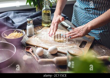 The woman is rolling out fresh dough for making pasta in a cozy atmosphere. Concept of cooking tasty food at home Stock Photo