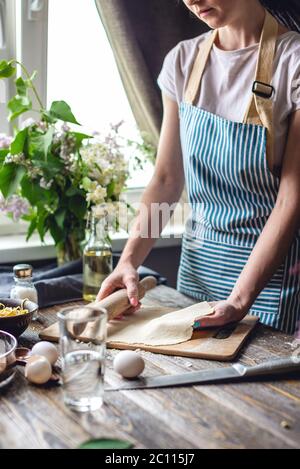 The woman is rolling out fresh dough for making pasta in a cozy atmosphere. Concept of cooking tasty food at home Stock Photo