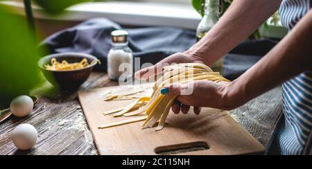 Woman is carefully holding raw fresh homemade noodles in her hands. Concept of process of cooking handmade pasta in a cozy atmosphere Stock Photo