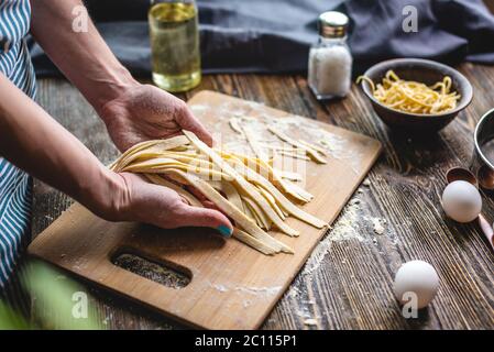 Woman is carefully holding raw fresh homemade noodles in her hands. Concept of process of cooking handmade pasta in a cozy atmosphere Stock Photo