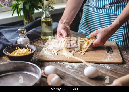 Woman is carefully holding raw fresh homemade noodles in her hands. Concept of process of cooking handmade pasta in a cozy atmosphere Stock Photo