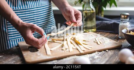 Woman is carefully holding raw fresh homemade noodles in her hands. Concept of process of cooking handmade pasta in a cozy atmosphere Stock Photo