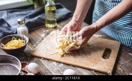 Woman is carefully holding raw fresh homemade noodles in her hands. Concept of process of cooking handmade pasta in a cozy atmosphere Stock Photo