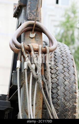 Metal ropes, hanging on its hinges behind the cab of a crane   background  black tires. Stock Photo