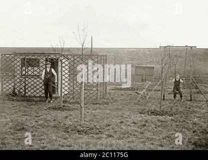 Two men resting from their digging on a smallholding or market garden in the Lincolnshire Wolds, England, UK c. 1900. One is on a swing. The same two men can be seen at work in another photograph (Alamy ref: 2C04TDJ). Stock Photo