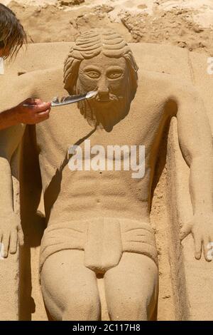 Young Man Working on Sand Sculpture of Jesus in Cadiz, Spain Stock Photo