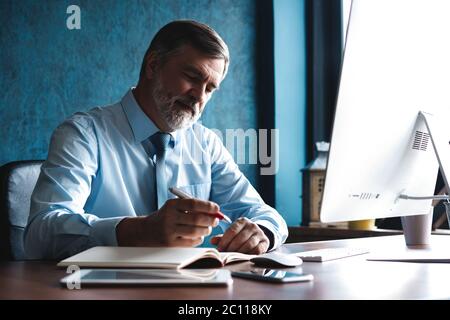 Mature businessman looking and analyzing document in his modern office at work. Stock Photo