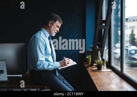 Concentrated at work. Focused mature businessman working and taking notes in his modern office. Stock Photo
