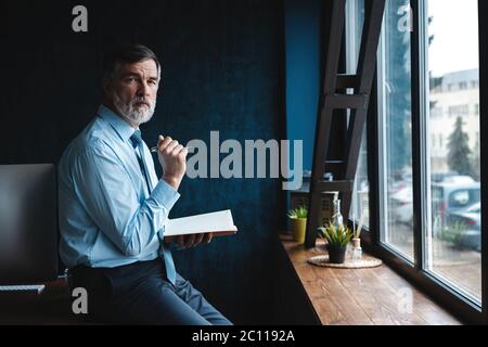 Concentrated at work. Focused mature businessman working and taking notes in his modern office. Stock Photo