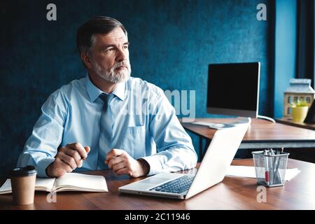 Focused mature businessman deep in thought while sitting at a table in modern office. Stock Photo