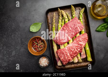 Raw Steak with green asparagus on tray on black background, top view Stock Photo