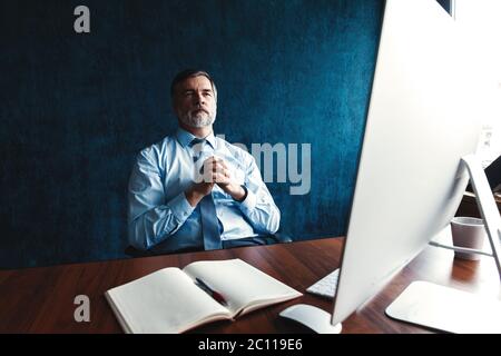 Focused mature businessman deep in thought while sitting at a table in modern office. Stock Photo