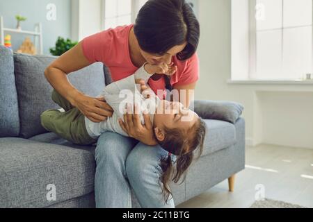 Happy mother and daughter hugging and playing on living room sofa. Family epidemic home isolation.