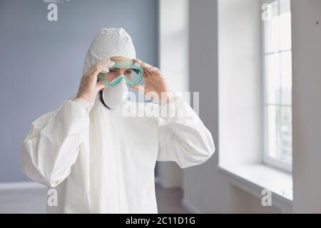 Male medicine specialist wearing PPE face mask and body protective suit putting on protection glasses Stock Photo